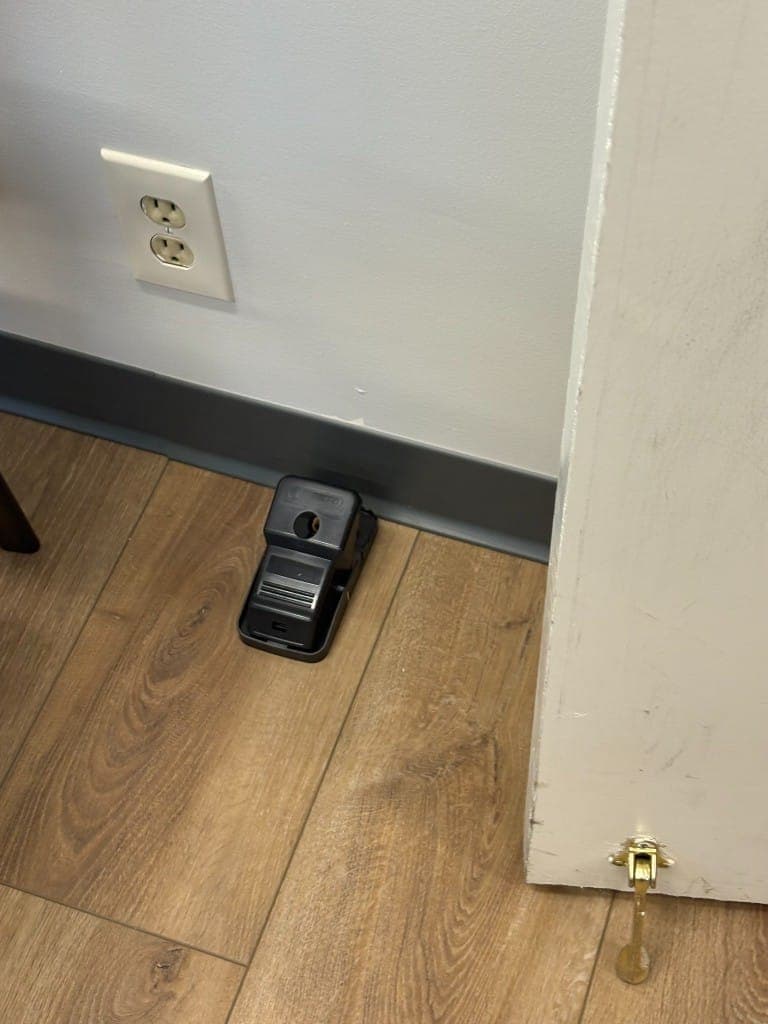 Tamper-resistant rodent station placed along an interior baseboard